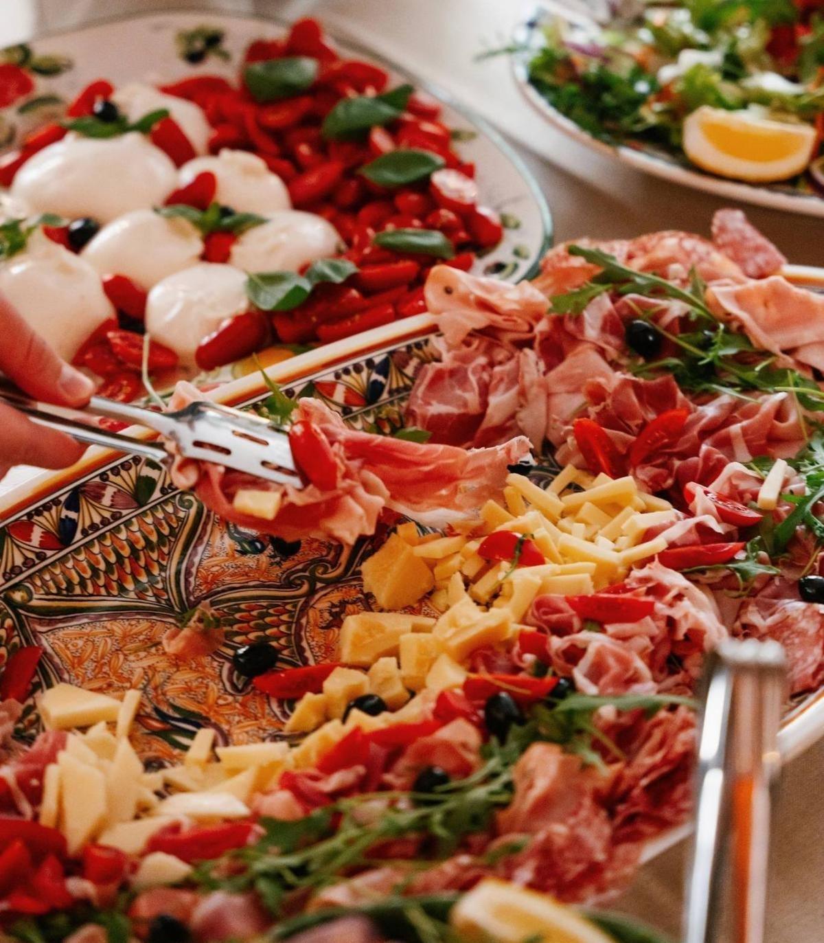 Antipasti with prosciutto, cheese and olives next to a mozzarella caprese